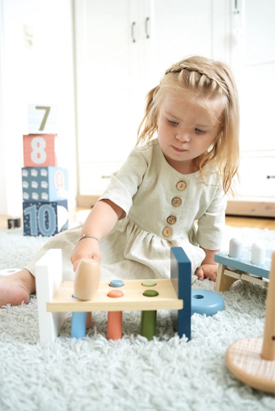 Meisje met blonde vlechtjes slaat met een houten hamer op pinnen.