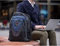 Zwarte rugzak naast een man in een jas die op een laptop typt.