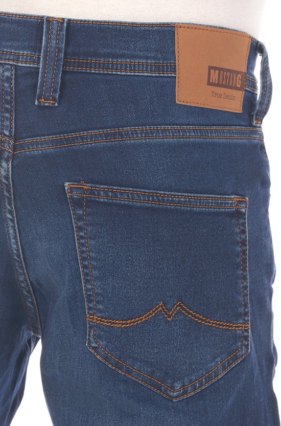 Detail van de achterkant van een donkerblauwe Mustang jeans met bruin leren label met 'Mustang True Denim'.