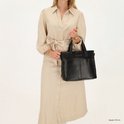 Vrouw met een zwarte leren tas in de hand, draagt een beige jurk.