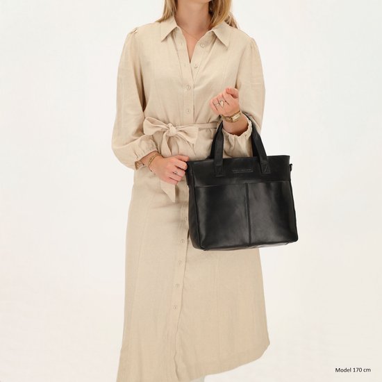 Vrouw met een zwarte leren tas in de hand, draagt een beige jurk.