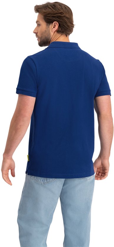 Man met zandkleurig haar, draagt een blauw NOMAD poloshirt met korte mouwen.