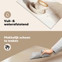 Wit en beige inductiebeschermer met een witte kop cappuccino, met een gesimuleerde waterplons. Een hand veegt de beschermer schoon met een grijze doek.