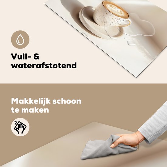 Wit en beige inductiebeschermer met een witte kop cappuccino, met een gesimuleerde waterplons. Een hand veegt de beschermer schoon met een grijze doek.