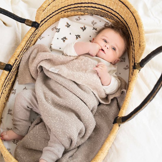 Baby in een rieten mand, draagt een gebroken wit shirt en taupe broekje, met een beige deken.