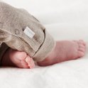 Detail van de voetjes van een baby in een beige boxpakje.