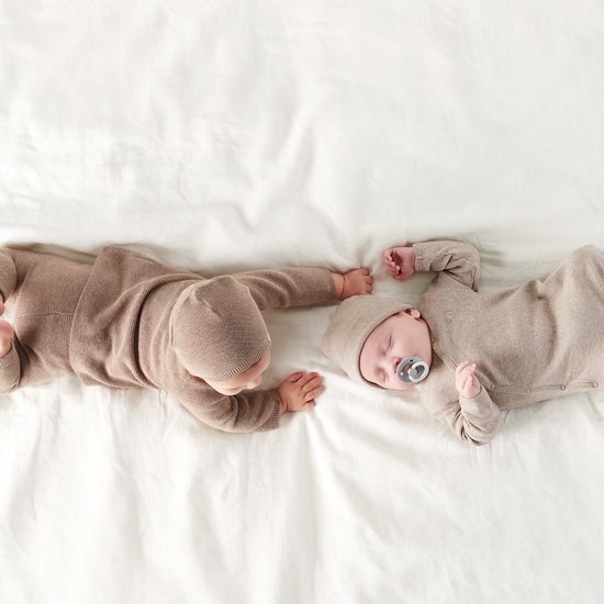 Twee baby's in bruine gebreide outfits, één met fopspeen.