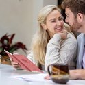 Een koppel in de woonkamer, de vrouw houdt een roze budget planner vast en lacht naar de man.