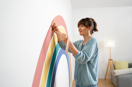 Vrouw met bruin haar brengt tape aan op een muur met een gekleurde regenboog.