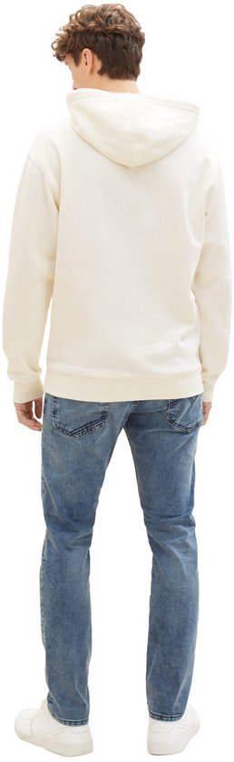 Man van achteren gezien in crème hoodie en blauwe jeans.