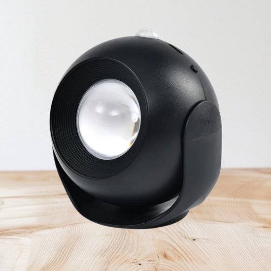 Zwarte bolvormige nachtlamp met lens, staand op een houten oppervlak.