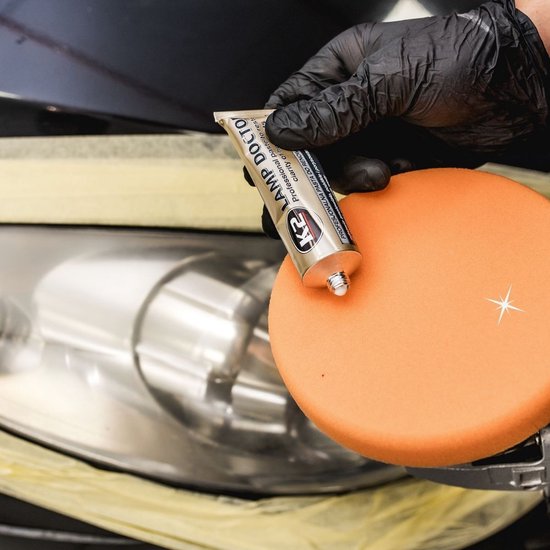 Een hand met een zwarte handschoen houdt een tube K2 Lamp Doctor omhoog, met een oranje polijstpad ernaast.