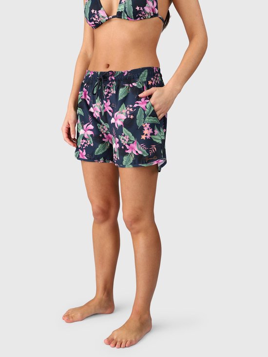 Mannequin portant un short de bain bleu foncé avec imprimé tropical, fleurs roses et feuilles vertes. Taille élastique avec cordon de serrage.