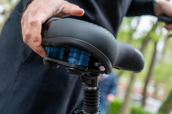 Dichtbij opname van de onderkant van een zwart fietszadel met blauwe elastomeer vering.