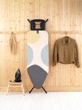 Strijkplank met stippenpatroon in geel, lichtblauw en grijs, staand tegen een houten wand.