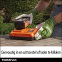 Twee handen met groene handschoenen wisselen een 20V/40V Dual Power accu buiten uit.
