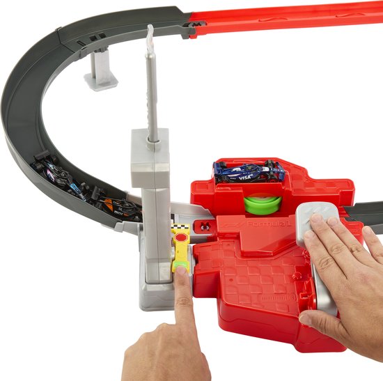 Hand bedient de lanceerder van de Hot Wheels F1 racebaan, met auto's op de baan en in de startpoort.