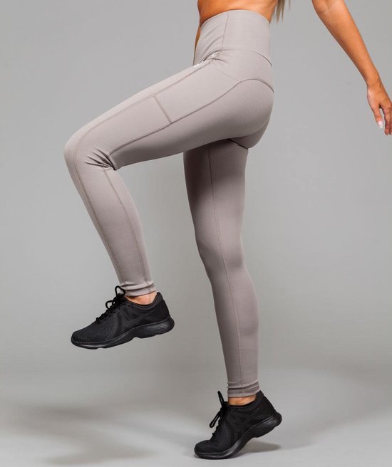 Lichtgrijze sportlegging met naden en zakken, gedragen door een vrouw met zwarte sportschoenen.