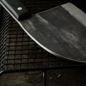 Close-up van het metalen lemmet van een slagersmes met een gebogen snede, geplaatst op een zwart rooster.