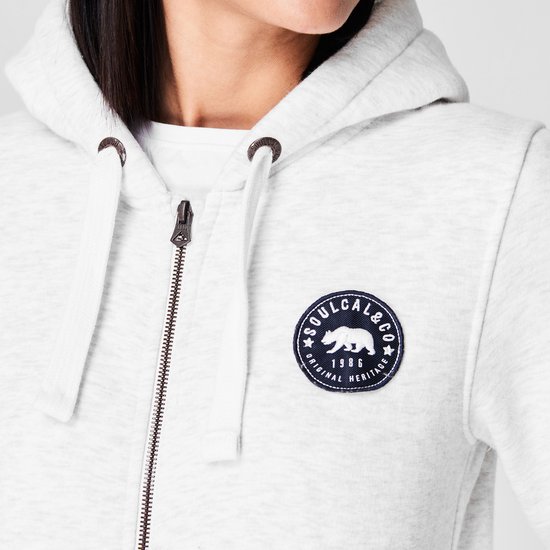 Close-up van de voorkant van een lichtgrijze dames hoodie met capuchon. Een badge met een beer en de tekst 'SOULCAL&CO ORIGINAL HERITAGE 1986' is zichtbaar.