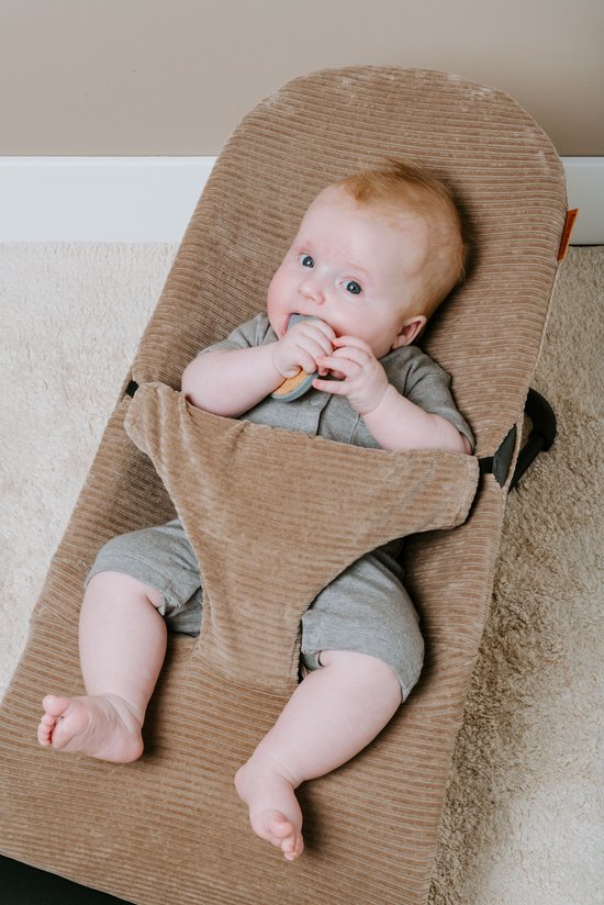 Baby met blauwe ogen en rood haar in een bruine corduroy wipstoel, sabbelt op een bijtring.