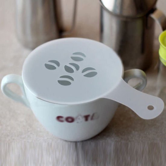 Wit koffie-stencil met vijf koffieboon-vormige openingen op een witte kop.