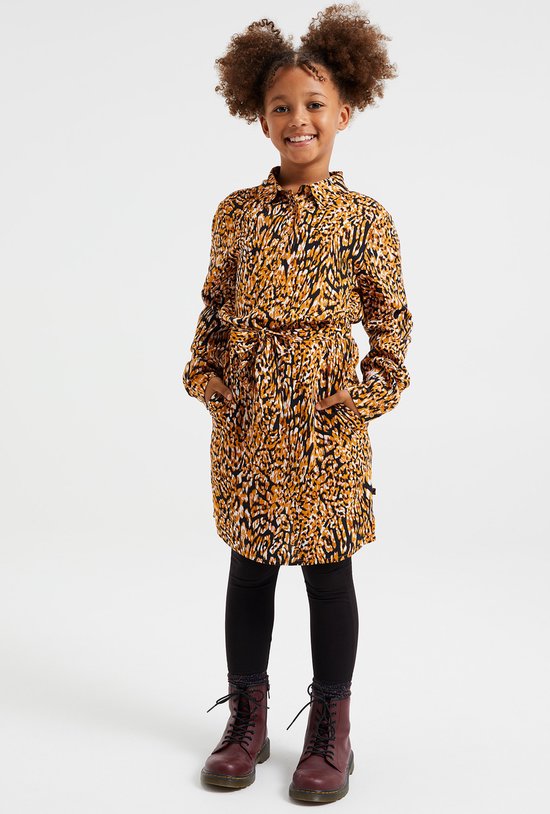 Meisje in een jurk met luipaardprint in bruin, geel en zwart, met ceintuur, gedragen over een zwarte legging.