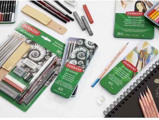 Detailopname van Derwent Academy kunstmaterialen. Een potlooddoos, een set schetspotloden in verpakking, en een schetsboek met potloden.