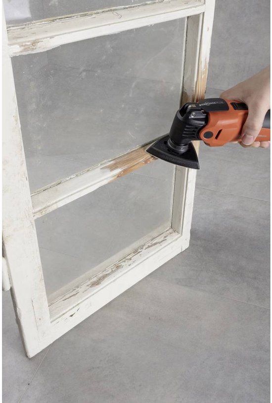 Oranje multitool met een driehoekige schuurzool die hout schuurt op een oud, wit raamkozijn.