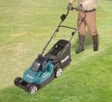Man met grasmaaier: een turquoise en zwarte Makita grasmaaier wordt gebruikt op een grasveld.