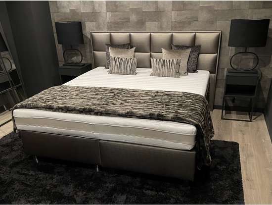 Luxe bed met bruin gestoffeerde boxen, wit matras, grijs gestreept hoofdbord en een faux bont sprei.
