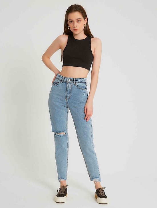Model draagt een lichtblauwe spijkerbroek met hoge taille, gescheurde knie, rafelige zoom. Zwarte crop top en sneakers.