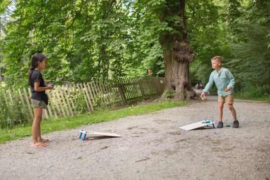 Jongen en meisje spelen cornhole met houten boards in een bosrijk gebied.