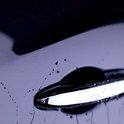 Gouttes d'eau sur la porte d'une voiture bleu foncé près d'une poignée de porte chromée.