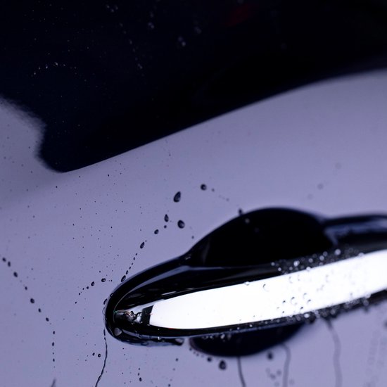 Gouttes d'eau sur la porte d'une voiture bleu foncé près d'une poignée de porte chromée.