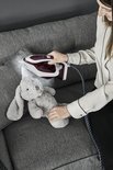 Vrouw strijkt een knuffelhaas met een bordeauxrood en wit strijkijzer op een bank.