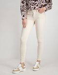 Model in een lichte, skinny jeans met rafels aan de onderkant en beige sneakers.