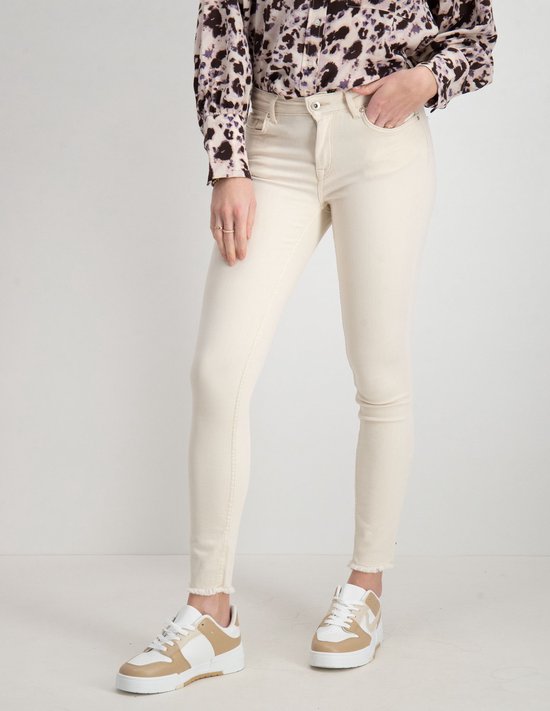 Model in een lichte, skinny jeans met rafels aan de onderkant en beige sneakers.