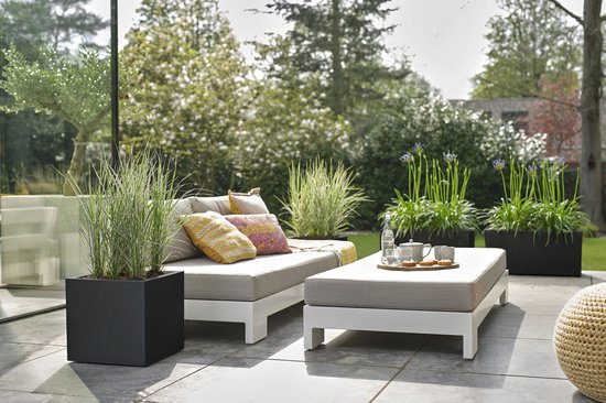 Luxe loungeset met witte bank en salontafel met kussens en planten in zwarte bakken.