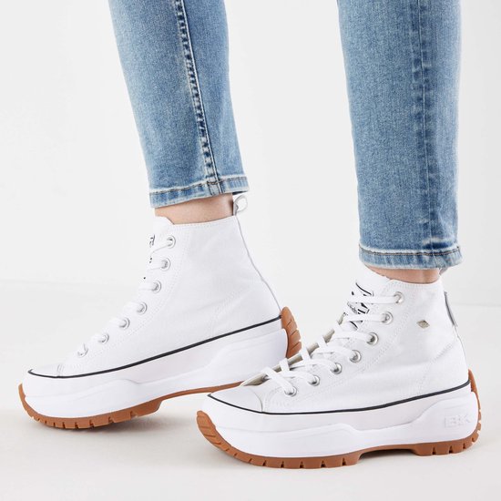 Damesvoeten in blauwe jeans met witte hoge canvas sneakers met dikke zolen.