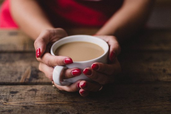 Vrouw met rode nagellak houdt witte mok met koffie vast.
