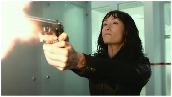 Maggie Q met zwart haar, vuurt een pistool af met vlammen uit de loop.