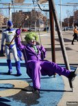 Een man als de Joker met groen haar en make-up, in een paars kostuum, zwaait op een schommel naast een man als Batman.