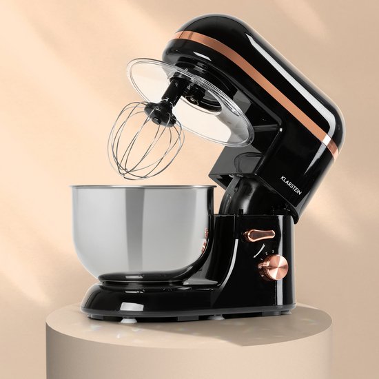 Zwarte keukenmachine met koperen details en zilveren kom, geplaatst op een verhoogd podium.