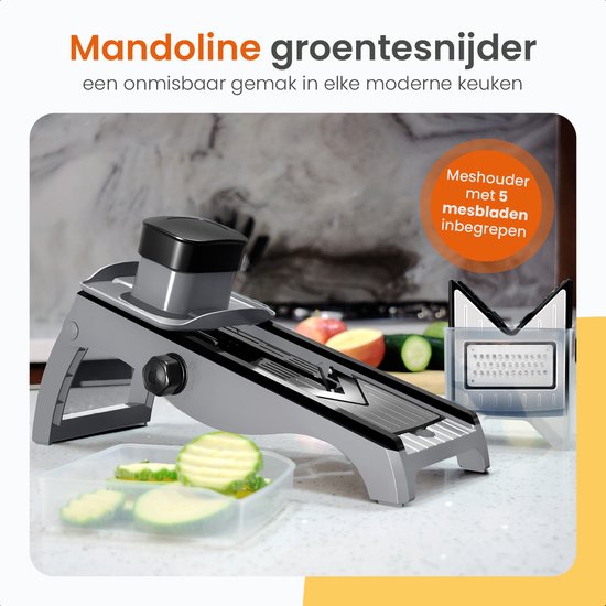 Grijze mandoline groentesnijder met meshouder en 5 mesbladen. Gesneden courgette ligt in een bakje. Een appel en komkommer liggen op de achtergrond.