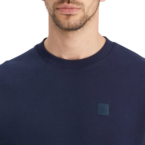 Close-up van donkerblauwe sweater met ronde hals en een vierkant logo met textuur.