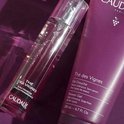 Caudalie douchegel in paarse tube en een verstuiver met paarse vloeistof, op paarse achtergrond.