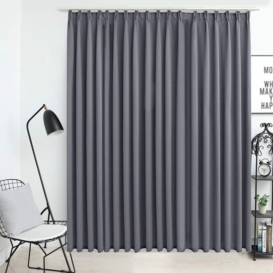 Grijze verduisterende gordijnen met fijne plooien, hangend voor een raam, naast een stoel met lamp.