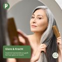 Oudere Aziatische vrouw met grijs haar kamt haar haar met een houten kam voor een spiegel.