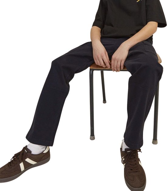 Zittende jongen in een zwarte cargobroek en bruine sneakers.